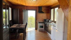 Una cabana de fusta amb zona de menjador, cuina i una porta corredissa de vidre que dona a un balcó.