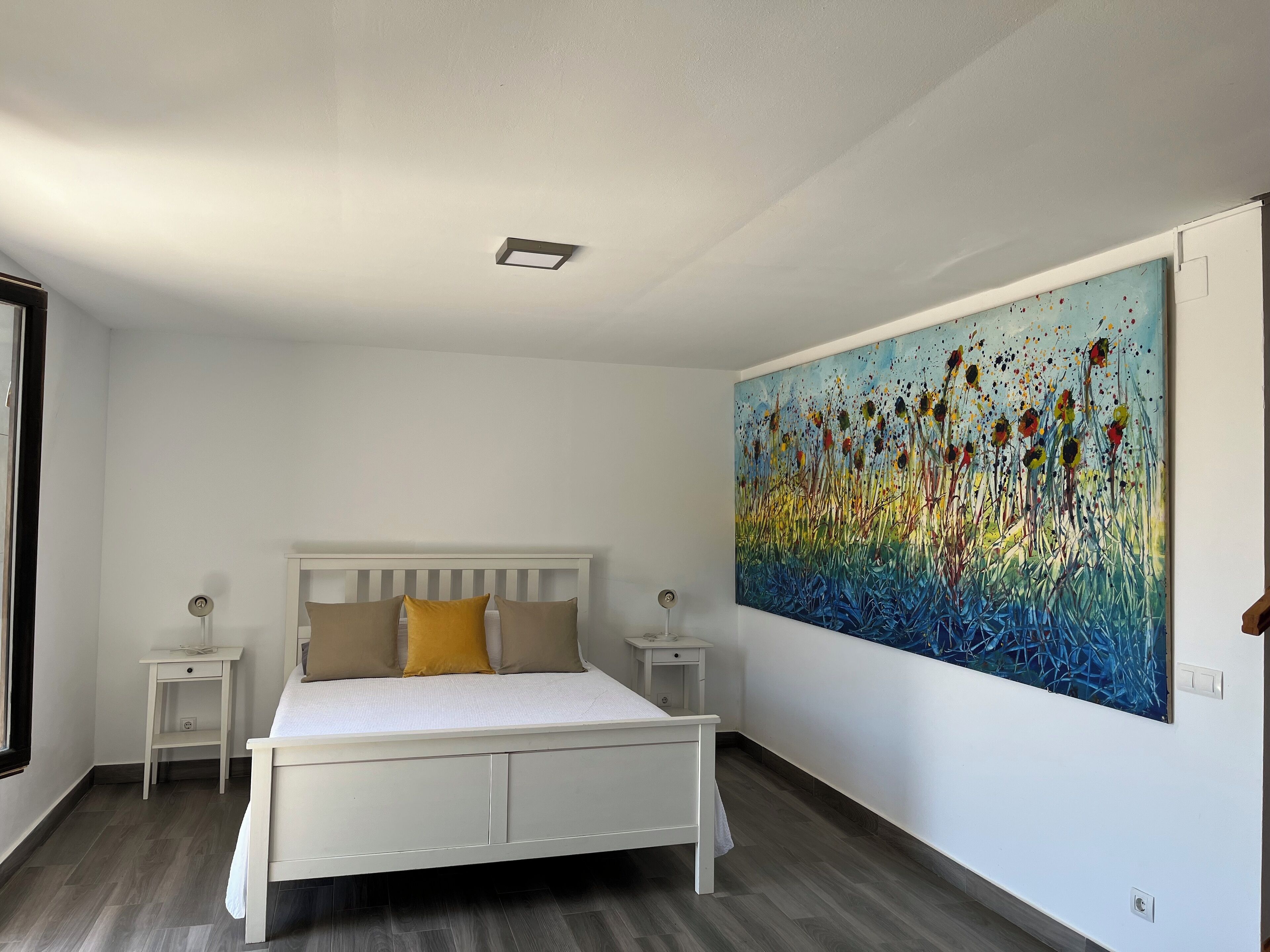 Een slaapkamer met een bed, nachtkastjes, een schilderij en een raam.