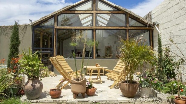 A greenhouse with a wooden frame, large glass windows, and a patio with chairs and potted plants. - Co404 San Cristobal (San Cristóbal de las Casas)