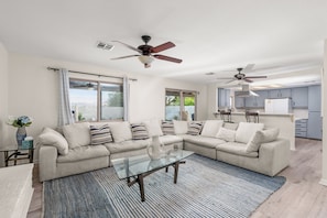 A modern living room with a sectional sofa, glass coffee table, and ceiling fans.