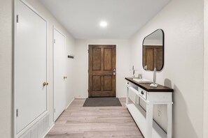 A hallway with a wooden door, a white vanity with a mirror, and a white cabinet.