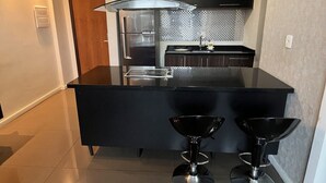 Une cuisine moderne dotée d’un îlot central, d’appareils électroménagers en acier inoxydable et de tabourets de bar noirs.