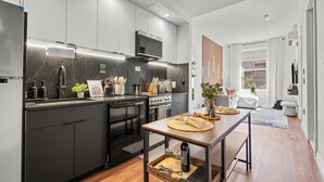 Una cocina moderna con armarios negros, un refrigerador de acero inoxidable y una mesa de comedor de madera.
