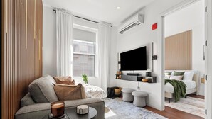 Una sala de estar moderna con sofá, una mesa de centro, televisión y una cama al fondo.