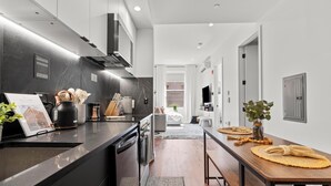 Una cocina moderna con encimera negra, electrodomésticos de acero inoxidable y una mesa de comedor de madera con un mantel tejido.
