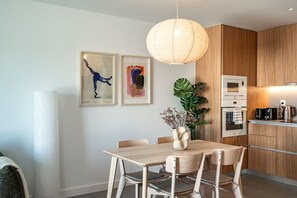 A modern kitchen with wooden cabinets, a dining table with chairs, and two framed artworks on the wall.