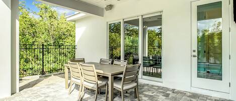 A patio with a table and chairs, a ceiling fan, and a glass door leading to a pool area.