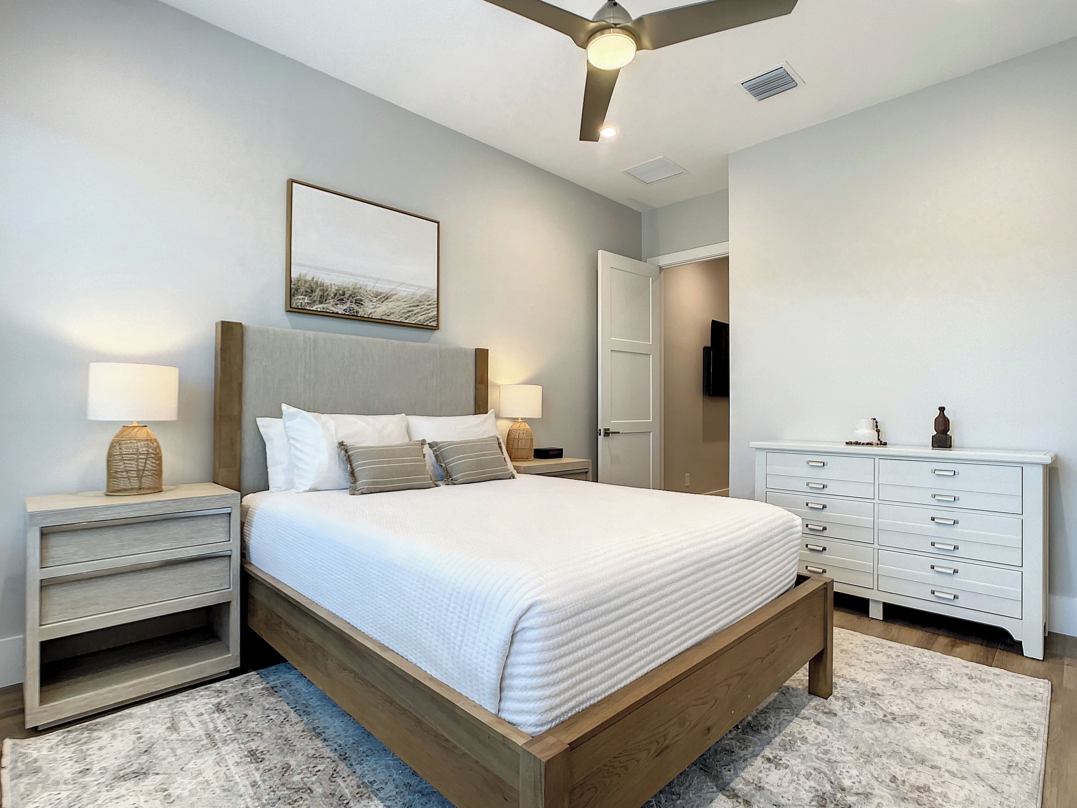 A bedroom with a bed, nightstands, a dresser, a ceiling fan, and a painting on the wall.