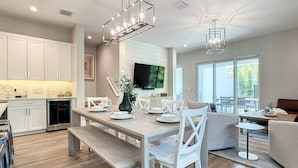 Een moderne keuken met witte kasten, een eethoek met witte stoelen, en een groot raam dat zorgt voor natuurlijk licht.