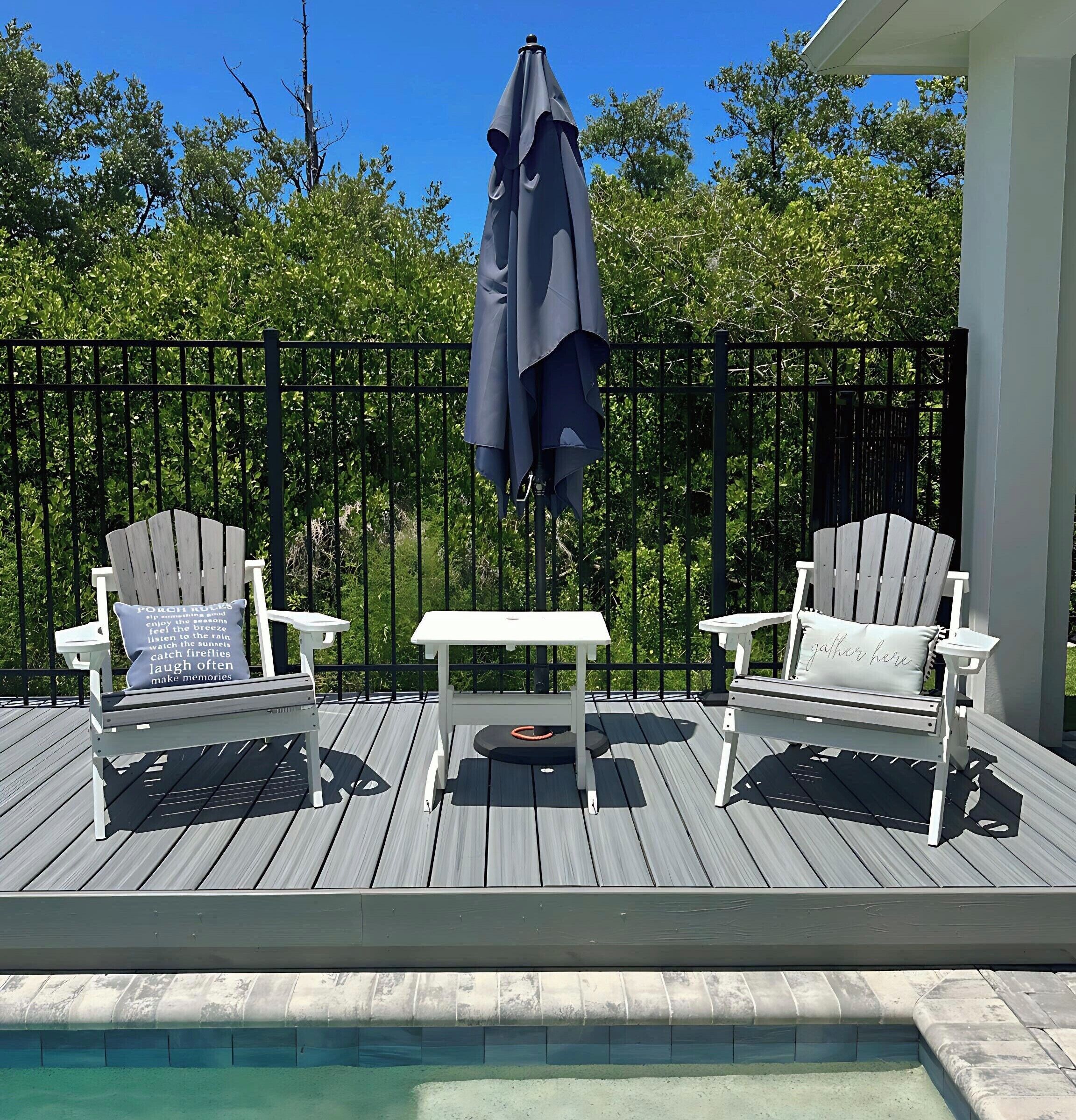 Eine Terrasse mit zwei Adirondack-Stühlen, einem kleinen Tisch und einem Pool.
