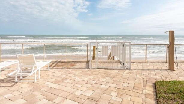 Une terrasse au bord de la plage, dotée de chaises longues et d’un espace salon abrité, offrant une vue sur l’océan.