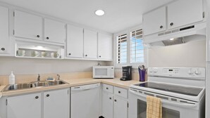 Una cocina con armarios blancos, microondas, cafetera y estufa.