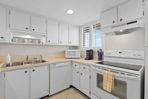 A kitchen with white cabinets, a microwave, a coffee maker, and a stove. - Ocean Club North C104 (New Smyrna Beach)