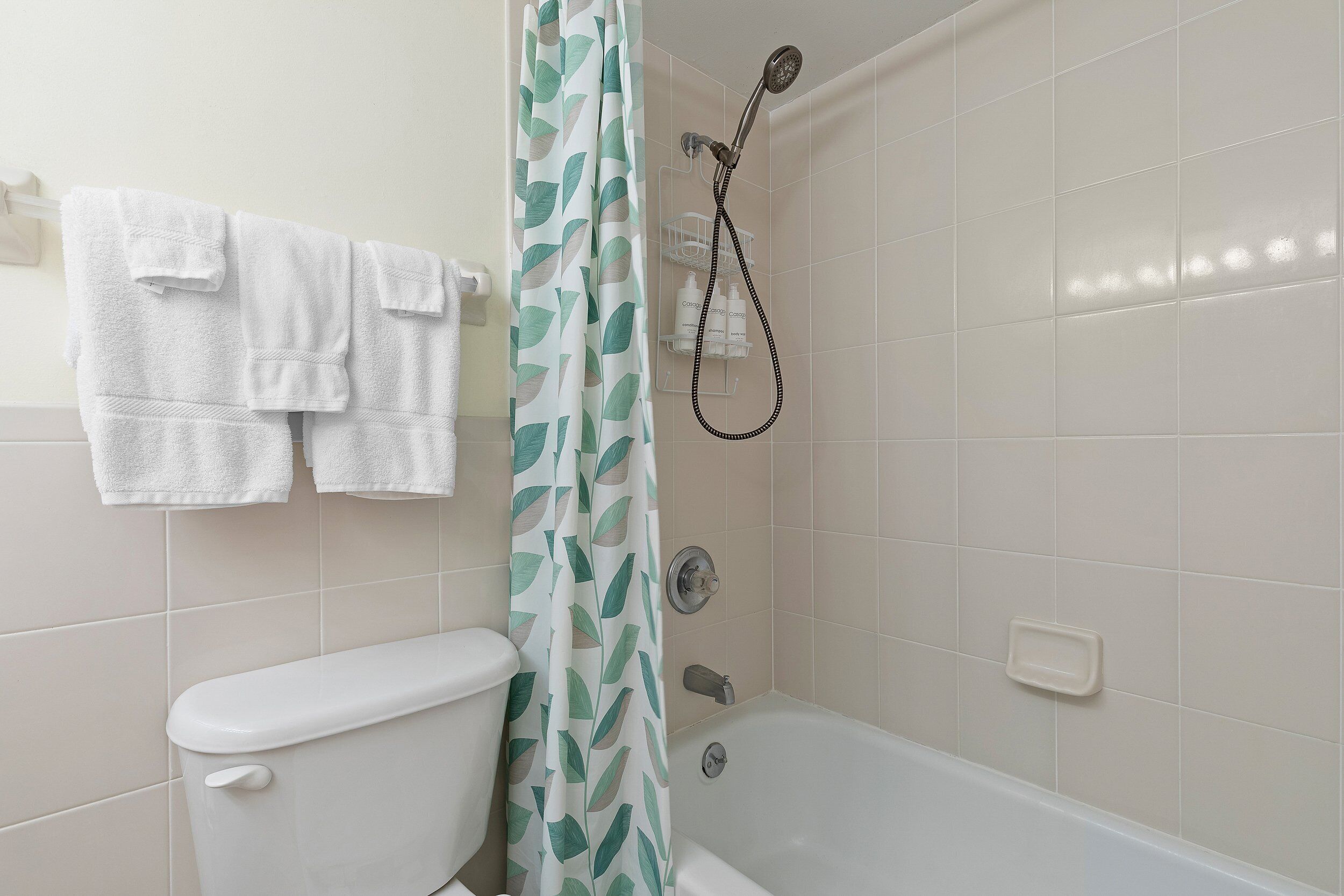 Un baño con inodoro, ducha con cortina de baño estampado con hojas verdes y bañera.