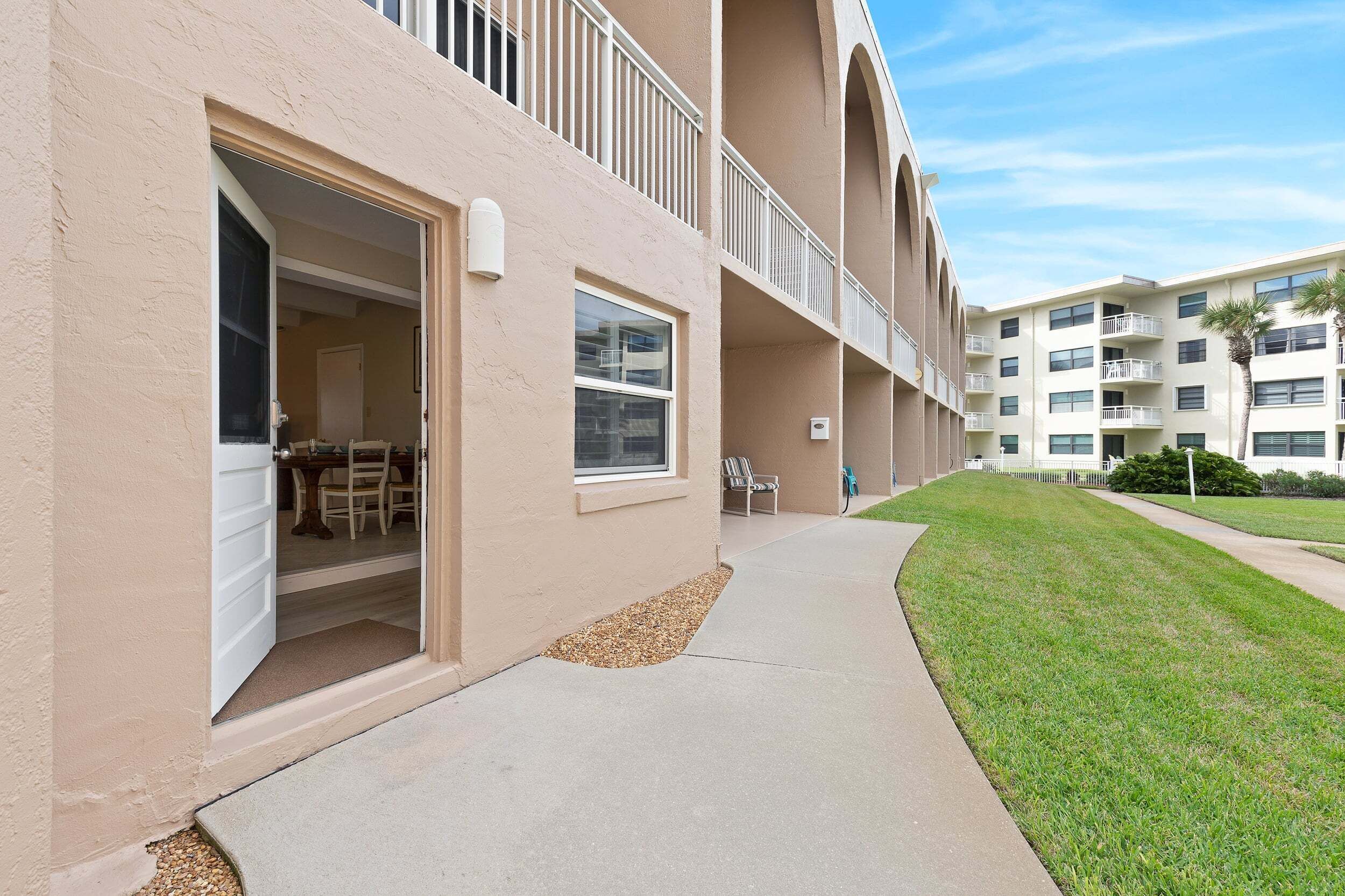 A multi-story building with balconies, a covered outdoor seating area, and a well-maintained lawn.