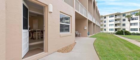 A multi-story building with balconies, a covered outdoor seating area, and a well-maintained lawn.
