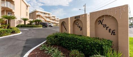 A building with balconies, a sign reading "4821 Club North," and a landscaped area with shrubs and plants.