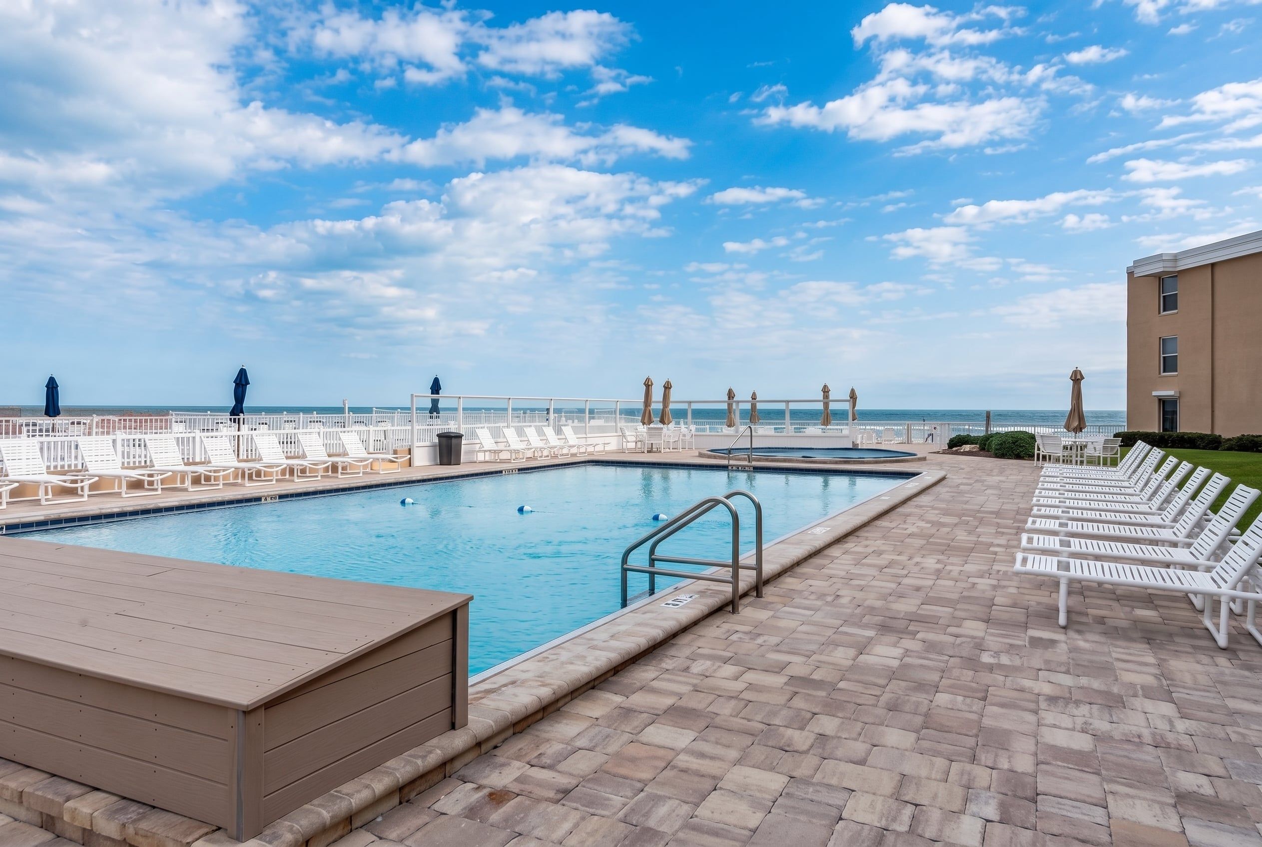 A pool area with lounge chairs and a view of the ocean.