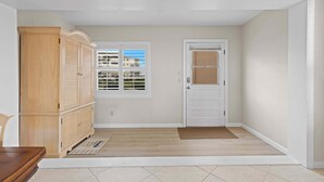 Un couloir avec une armoire en bois, une porte blanche et une fenêtre avec des stores.