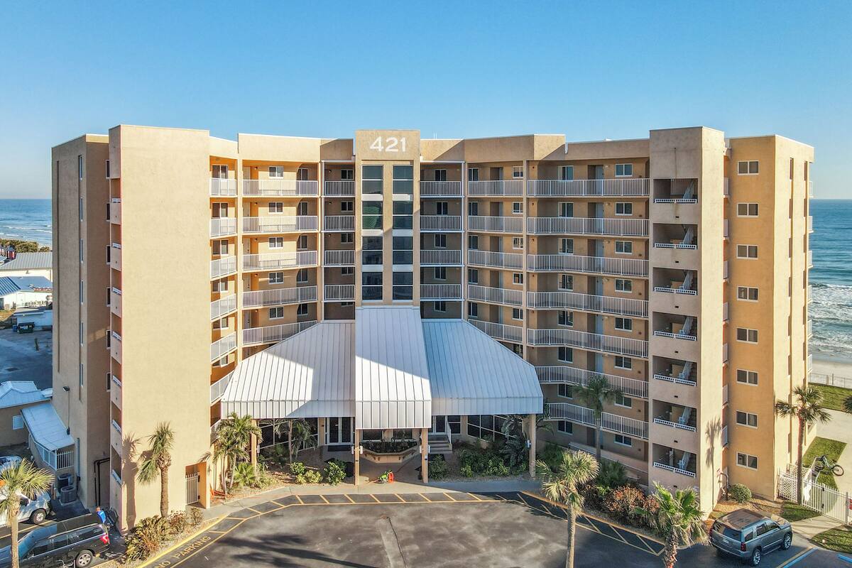 A multi-story hotel with a central atrium, numbered 421, featuring balconies, a parking area, and a view of the ocean.