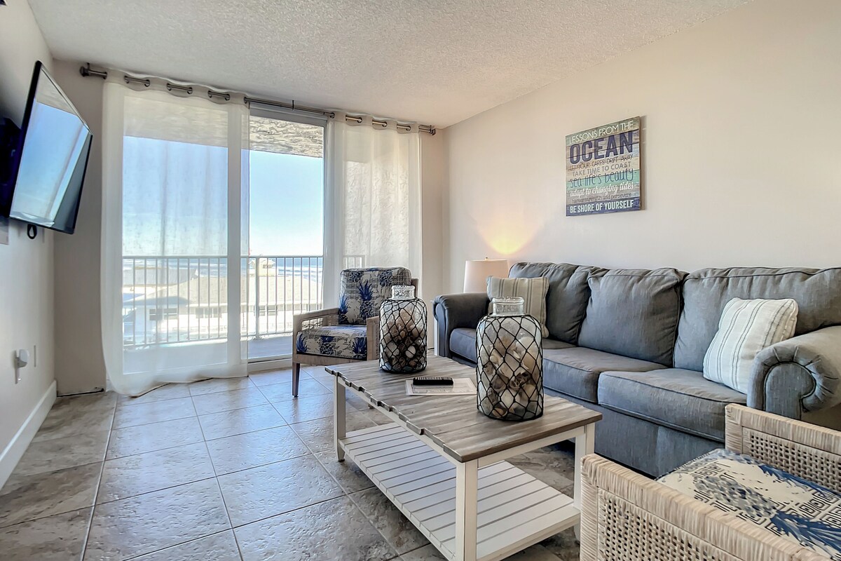 A living room with a grey sofa, a coffee table, and a TV mounted on the wall.