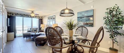 A dining area with wicker chairs, a glass table, and a potted plant.