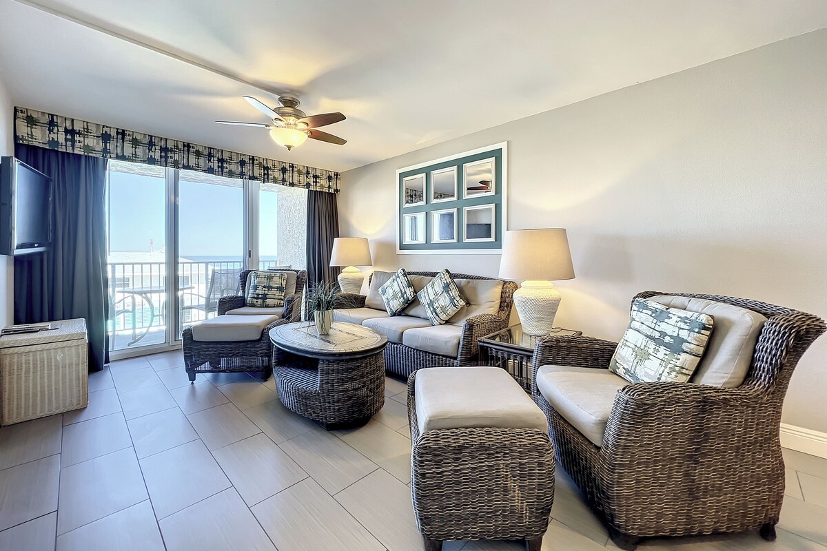 A spacious living room with wicker furniture, a ceiling fan, and a view of the outdoors.