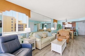 A living room with a sofa, armchair, and coffee table, a kitchen area with a dining table, and a visible door leading to another room. - Oceania Beach Club (New Smyrna Beach)