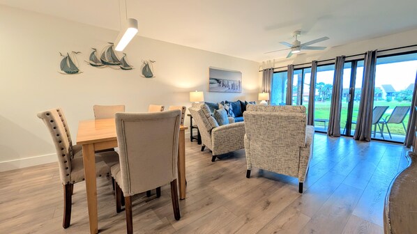 Un salon spacieux comprenant un coin repas, de grandes fenêtres et un ventilateur de plafond.