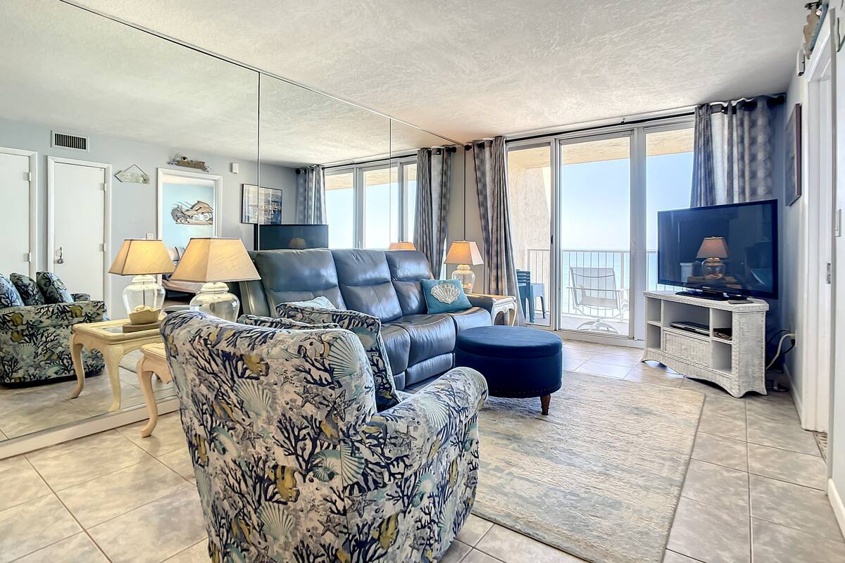 A living room with a sofa, armchairs, a TV, and a balcony with a view.