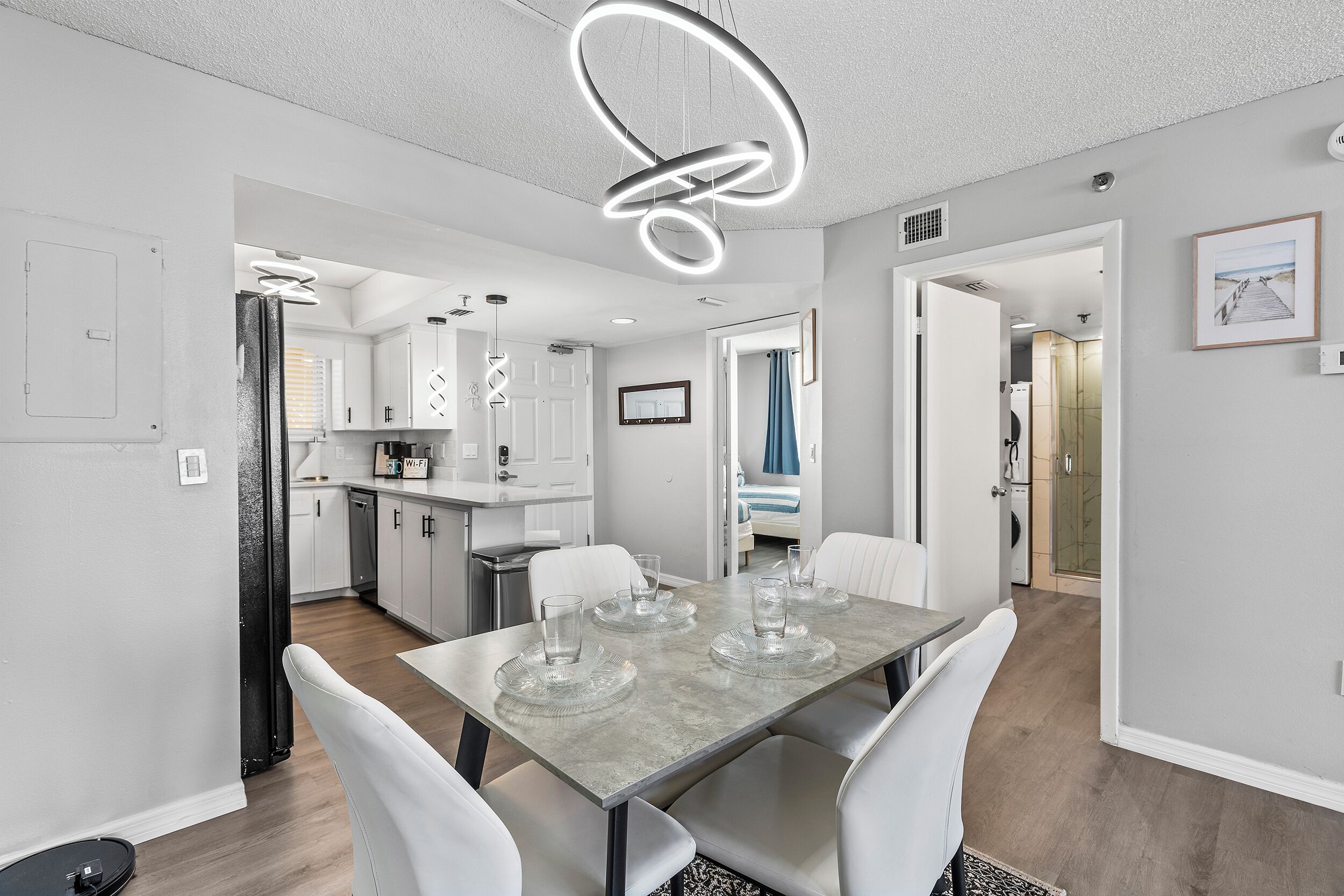 Une cuisine moderne avec des meubles blancs, une table à manger avec des chaises et un luminaire circulaire original.