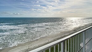 Vista de la playa con olas, cielo despejado y sol.