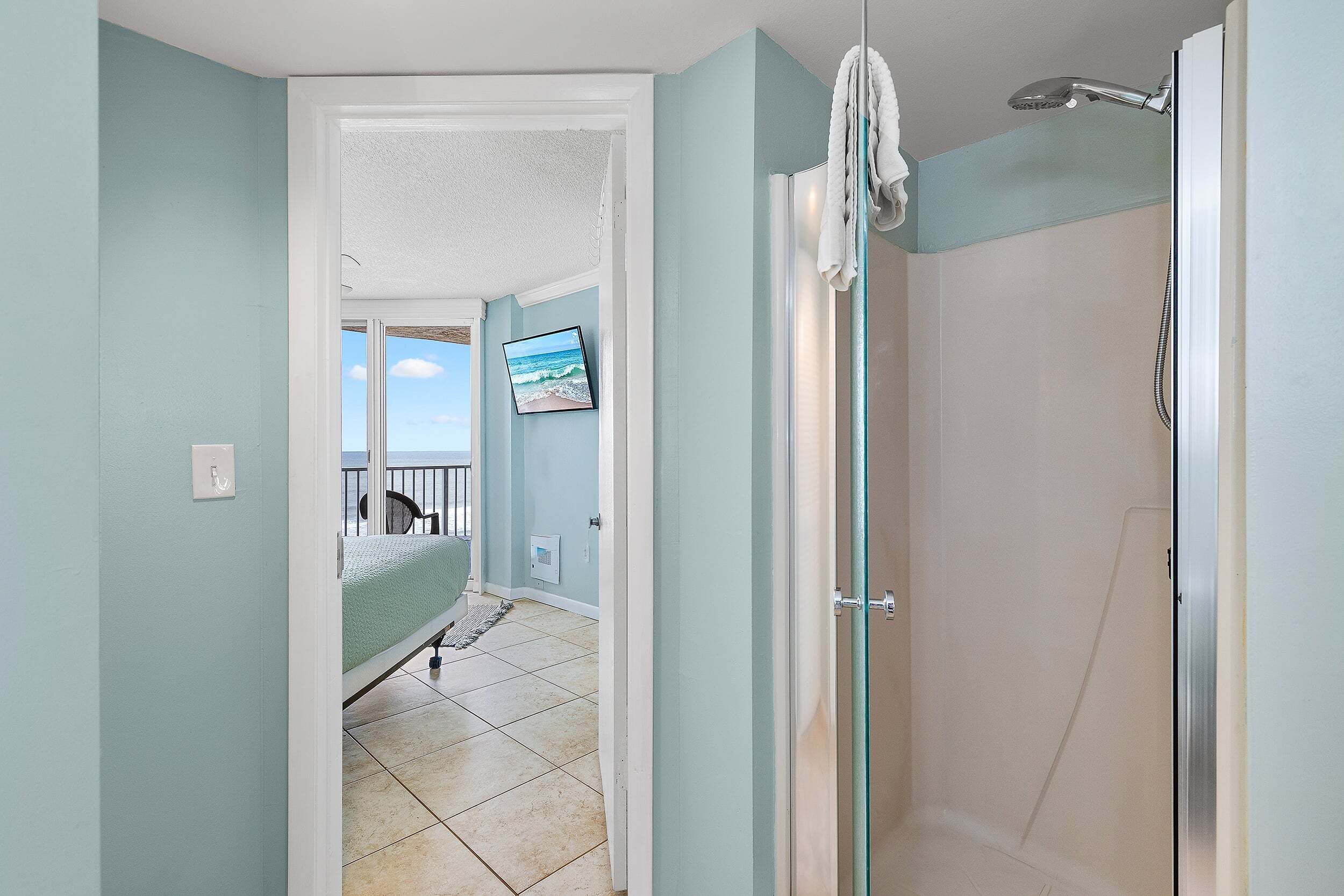 Une salle de bain avec douche, une porte donnant sur une chambre, et une vue sur le ciel par une fenêtre.