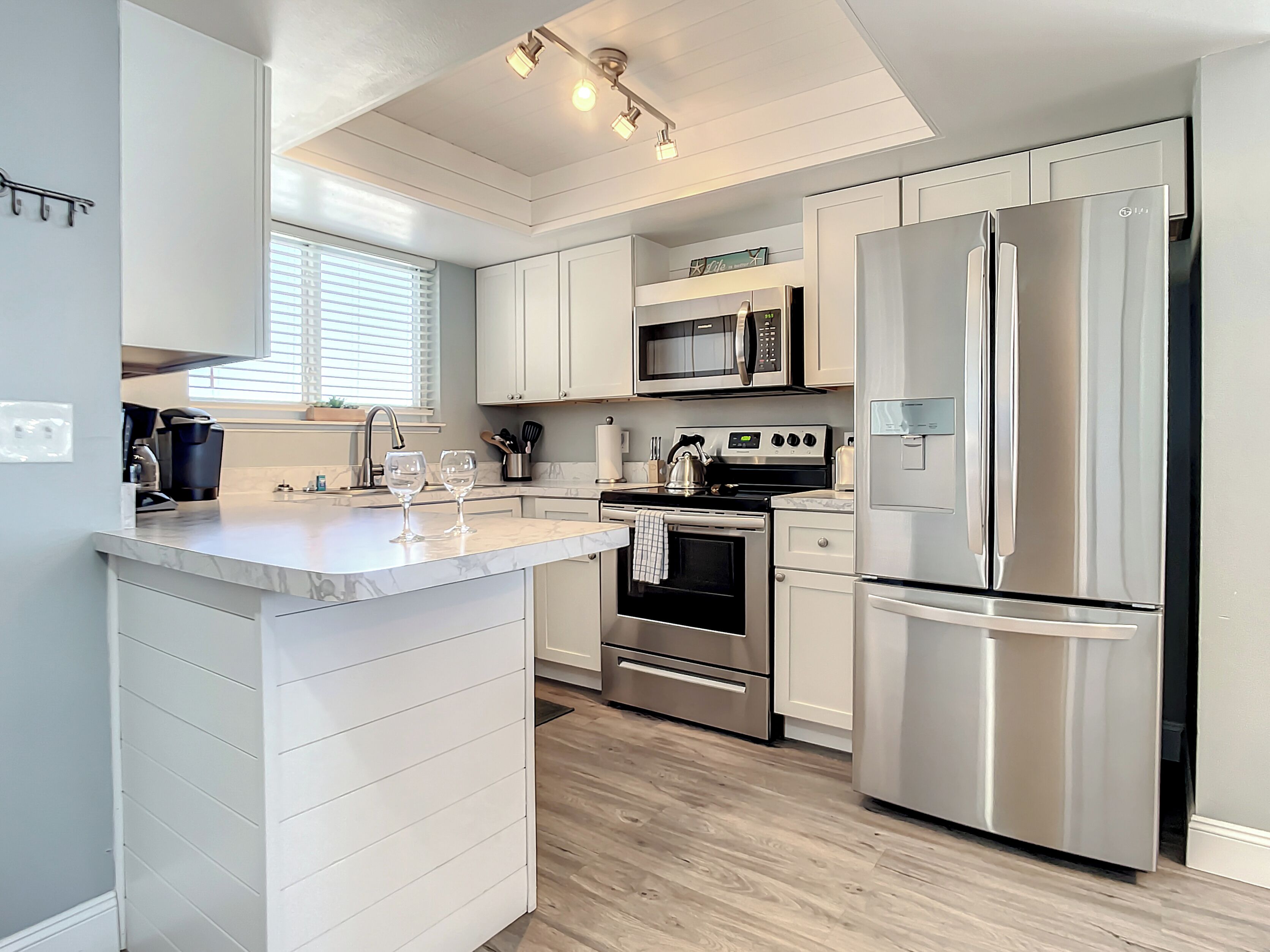 A modern kitchen with white cabinetry, stainless steel appliances, and a marble countertop.