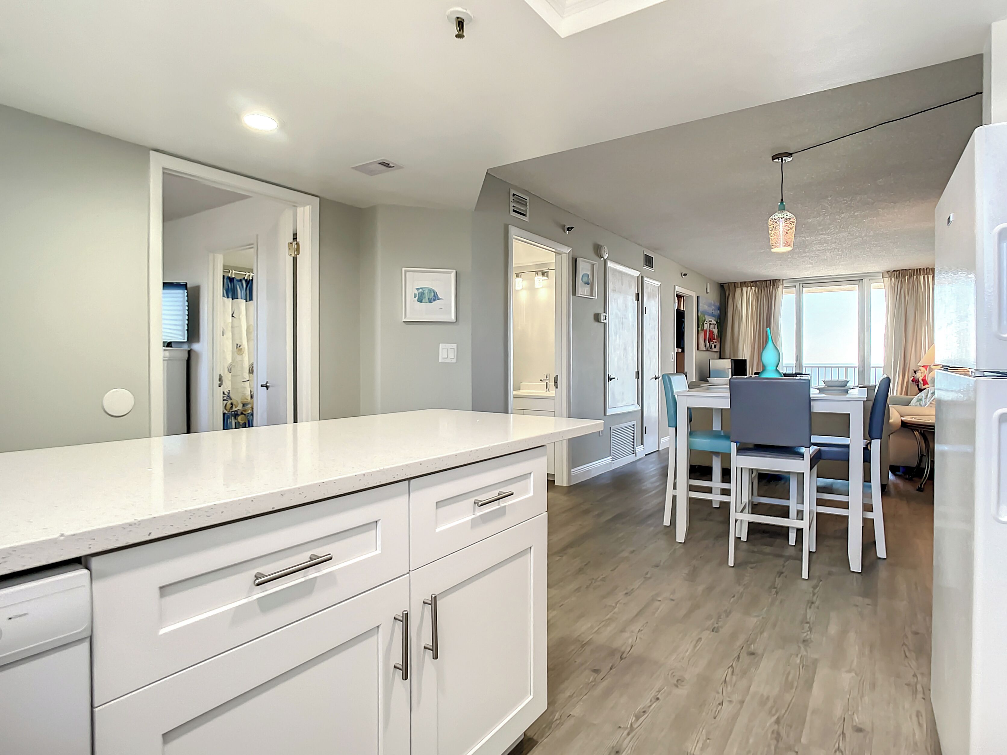 Une cuisine moderne avec des meubles blancs, un coin repas comprenant une table et des chaises, et une vue sur le salon grâce à une porte ouverte.