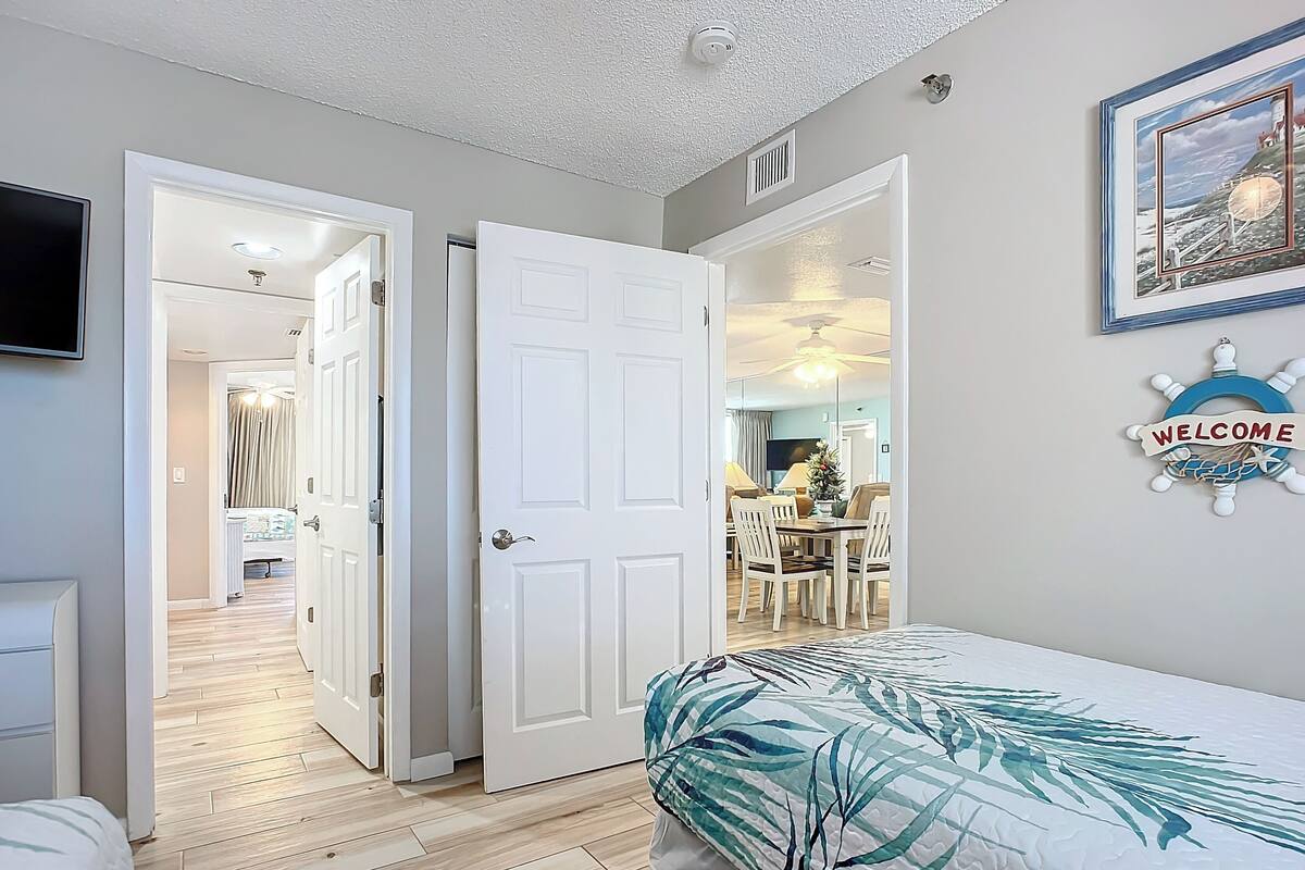 Un dormitorio con cama, una puerta que da a un comedor y un cartel que dice 'Welcome' en la pared.