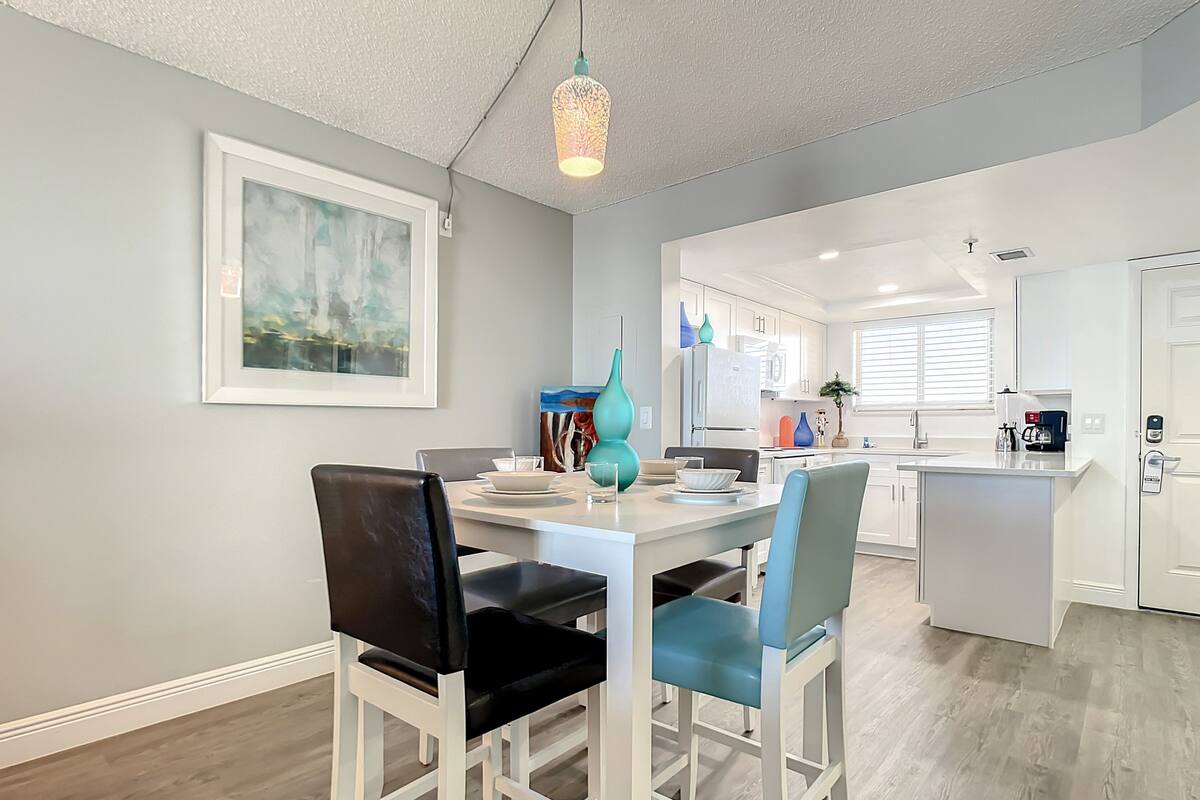 A modern kitchen with white cabinets, a central island, and a dining area with white chairs and a table.