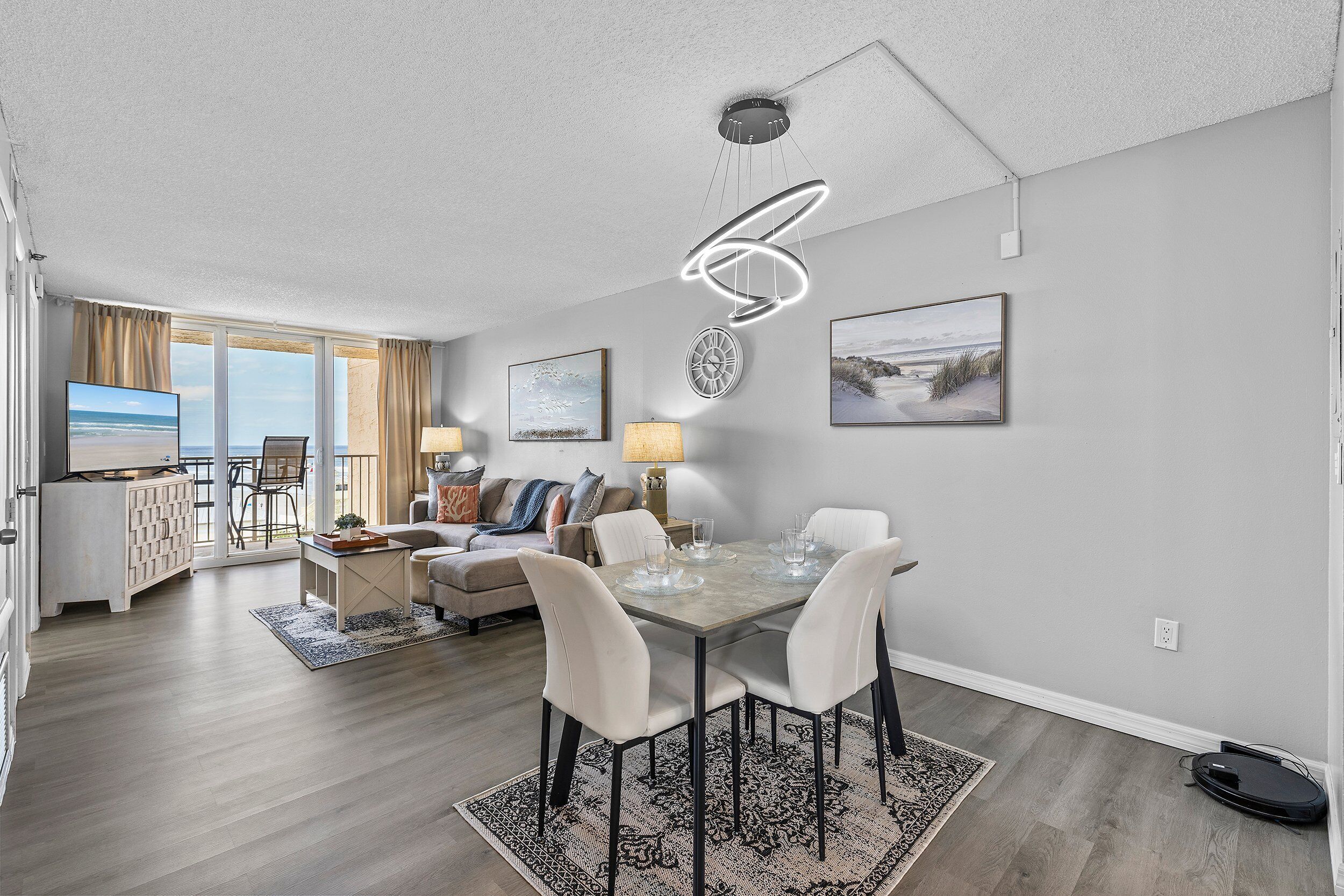 A modern living room with a dining area, large windows, and a ceiling light fixture.