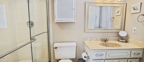 Une salle de bain avec une douche à parois de verre, des toilettes, un lavabo avec un meuble-vasque et un miroir avec éclairage.