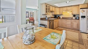 A kitchen with wooden cabinets, a refrigerator, and a dining area with a table and chairs. - Oceanside Village C1 (New Smyrna Beach)