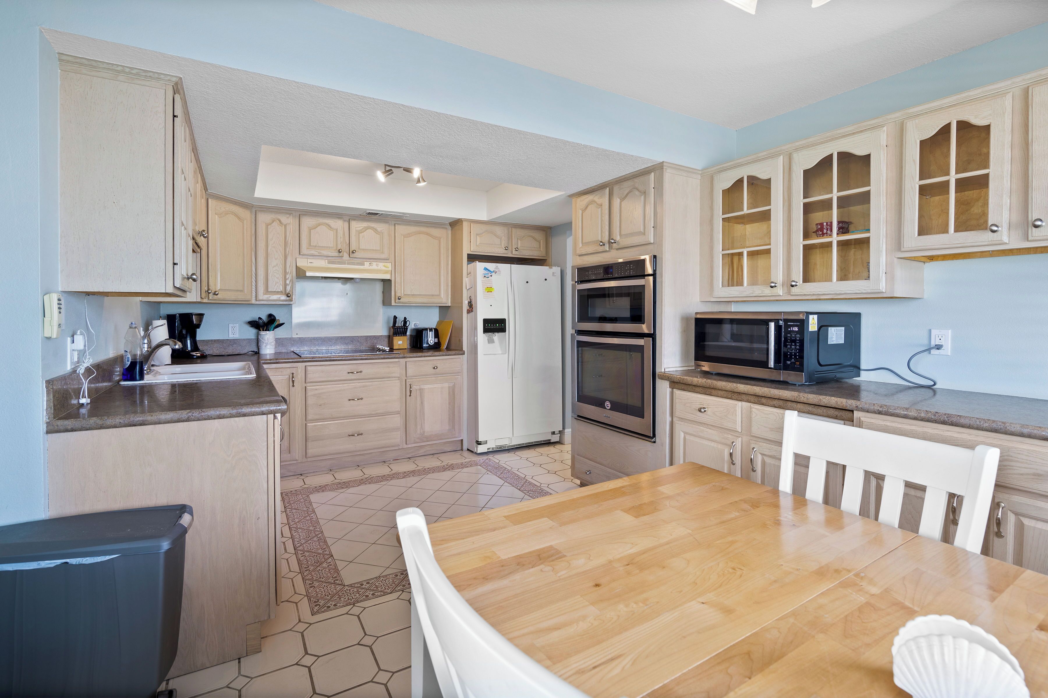 A kitchen with wooden cabinets, a refrigerator, an oven, a microwave, and a dining table with chairs.