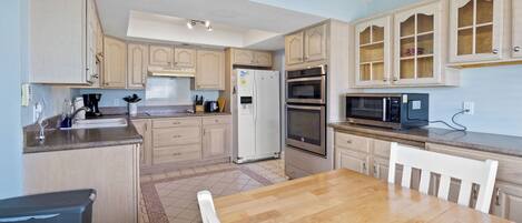 A kitchen with wooden cabinets, a refrigerator, an oven, a microwave, and a dining table with chairs.
