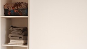 Un estante blanco con una caja estampada, toallas dobladas y un secador de pelo.
