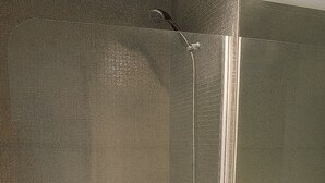 Un baño con un lavamanos blanco, un cabezal de ducha de mano y un espejo.