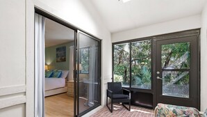 Una stanza con una porta a vetri scorrevoli che dà su un balcone, un letto con un comodino e una sedia.