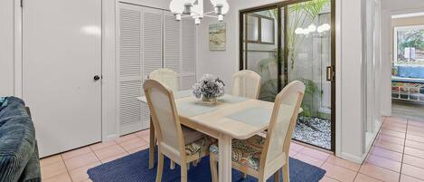 A dining area with a table, chairs, and a chandelier. There is a sliding glass door leading to a balcony with plants.