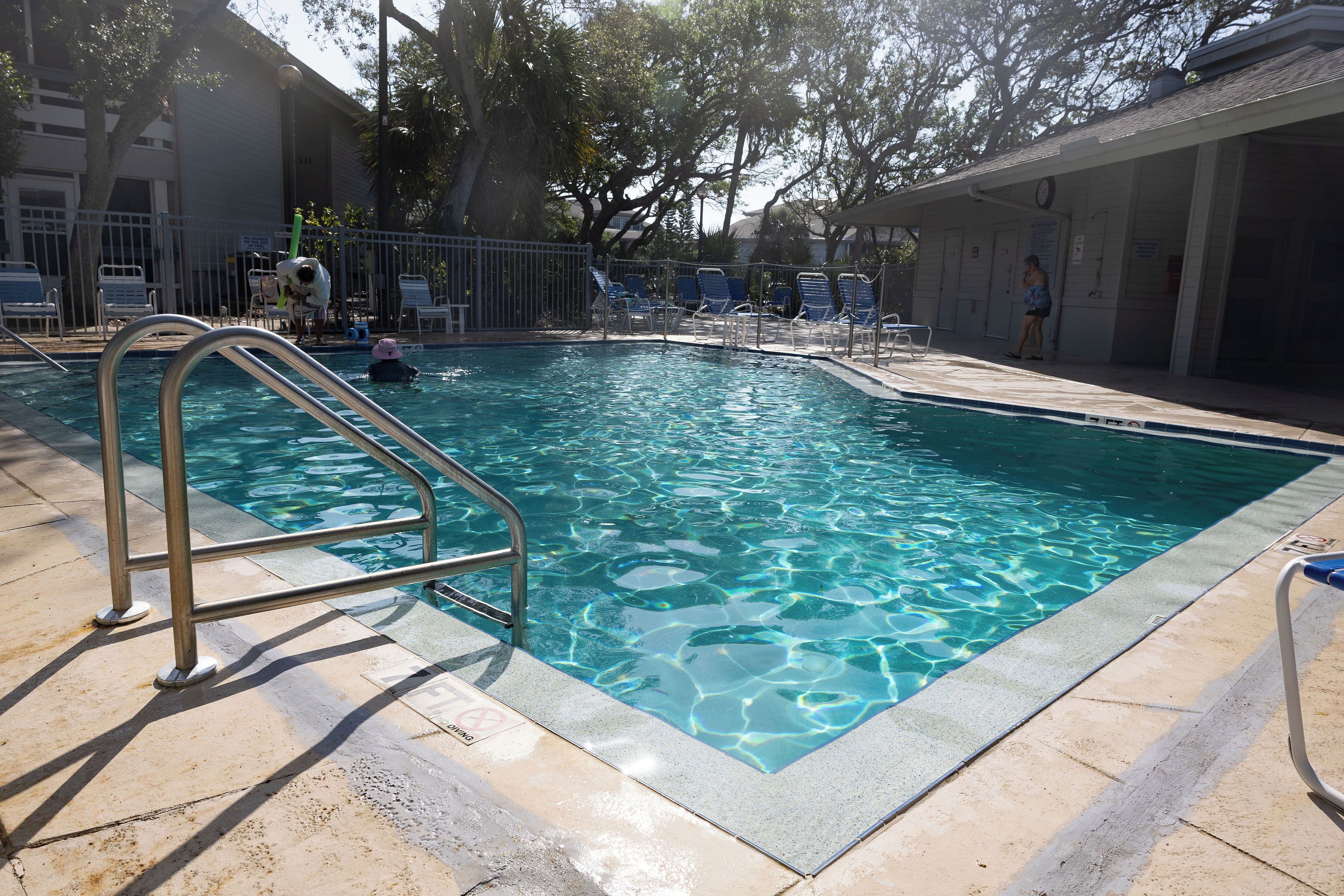 A swimming pool with a metal ladder, surrounded by lounge chairs and a covered area.