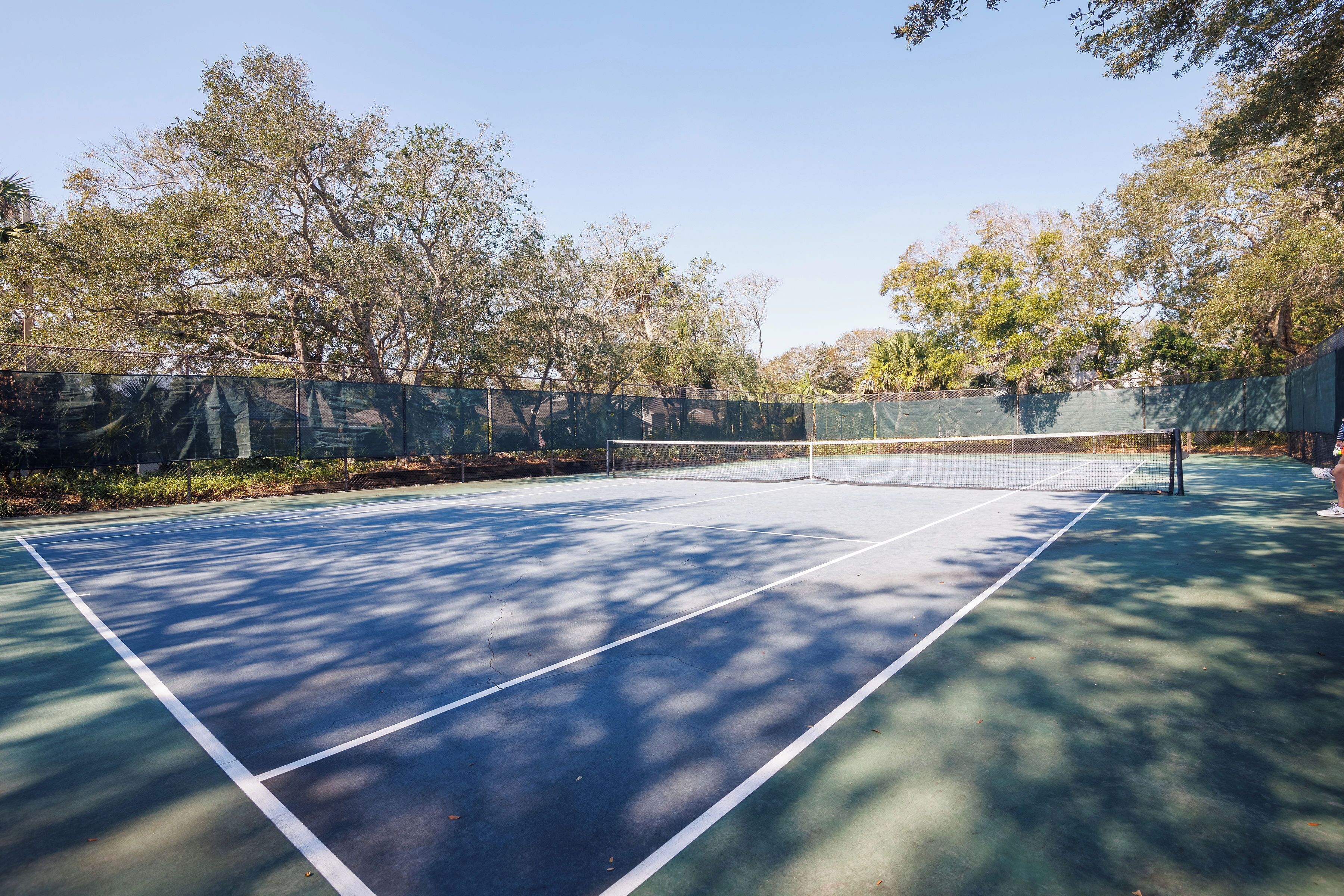 An outdoor tennis court surrounded by trees.