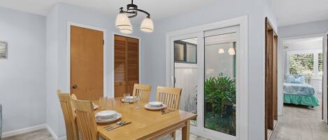 A dining area with a wooden table and chairs, a ceiling light fixture, and a sliding glass door leading to a garden.