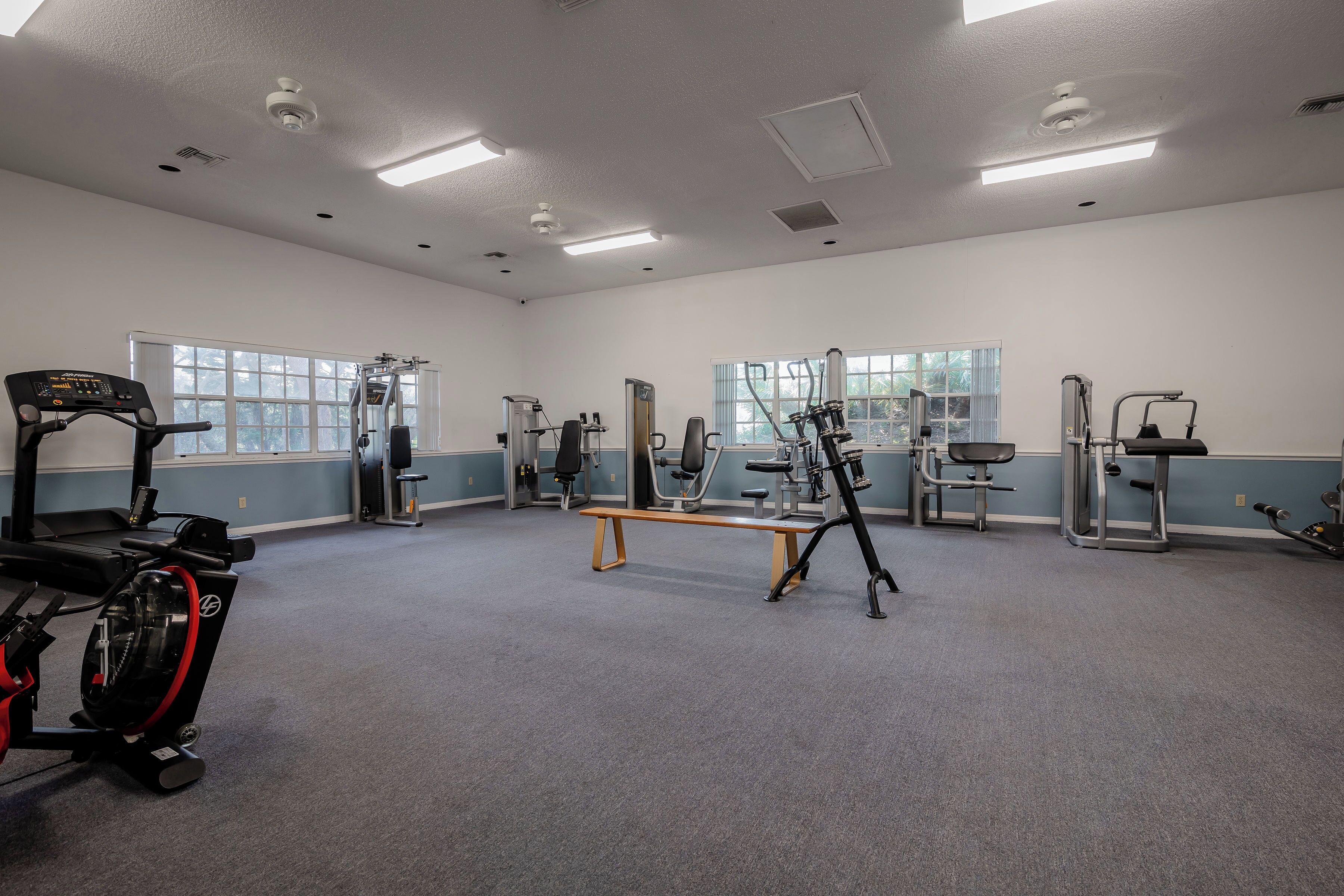 Een sportschool met diverse fitnessapparaten, grote ramen en een bank.